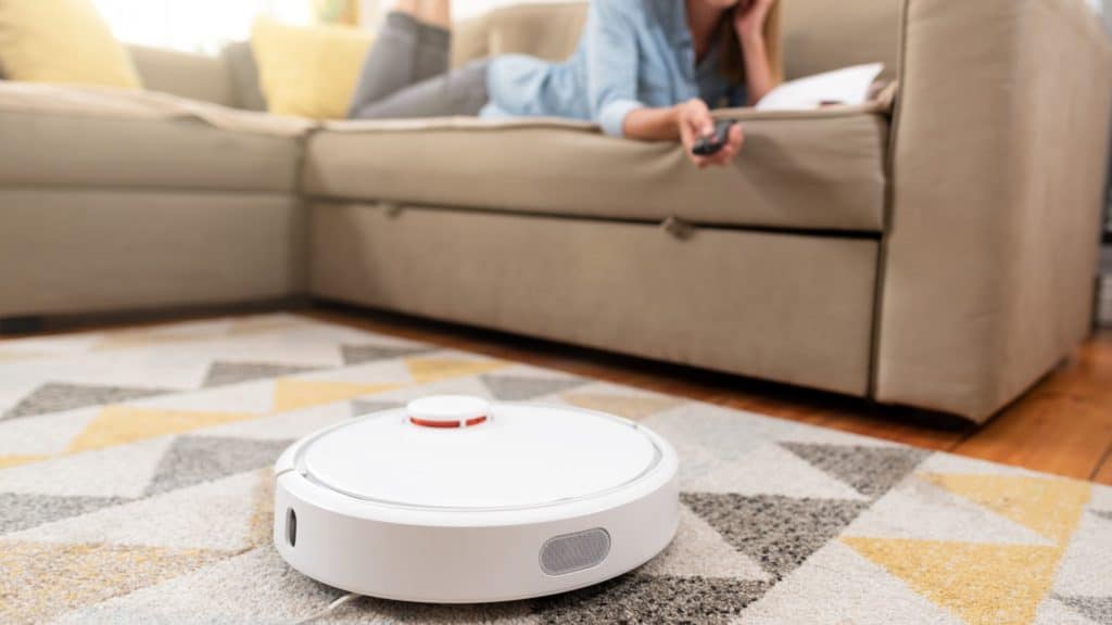 A lady on the couch with a robot vacuum. How to Keep Your Robot Vacuum from Going Under The Couch