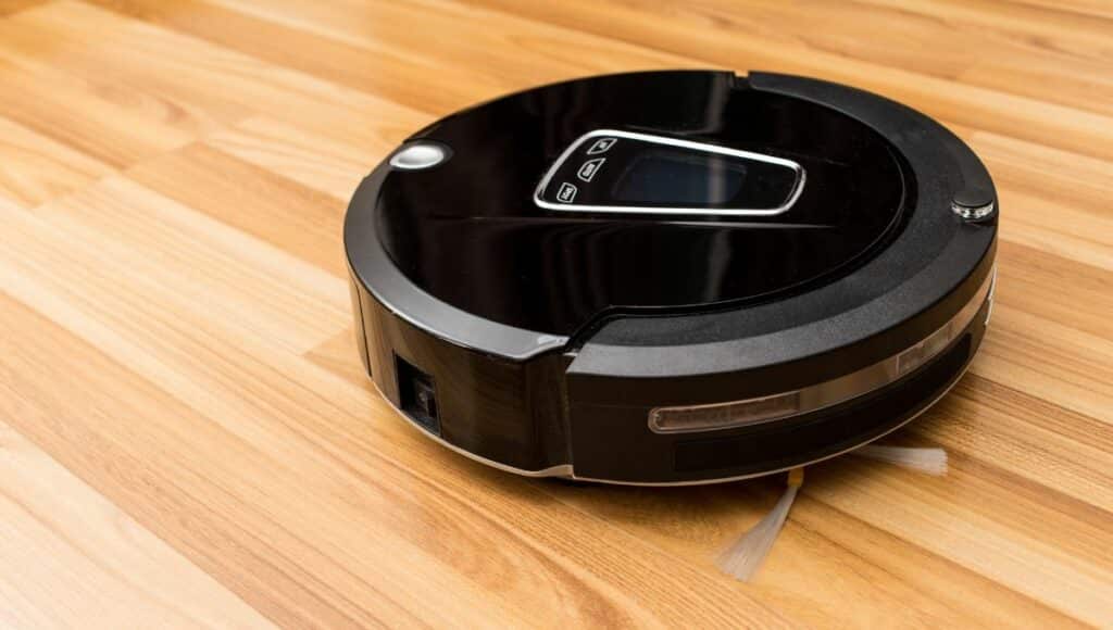A black automatic robot vacuum cleaner vacuuming on the wood floor