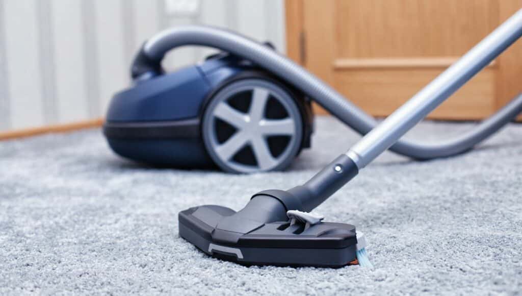 A blue regular stick vacuum cleaner on the carpet