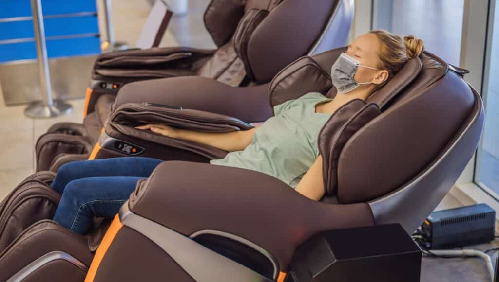 A beautiful young woman wearing a medical mask rests in a massage chair at the mall