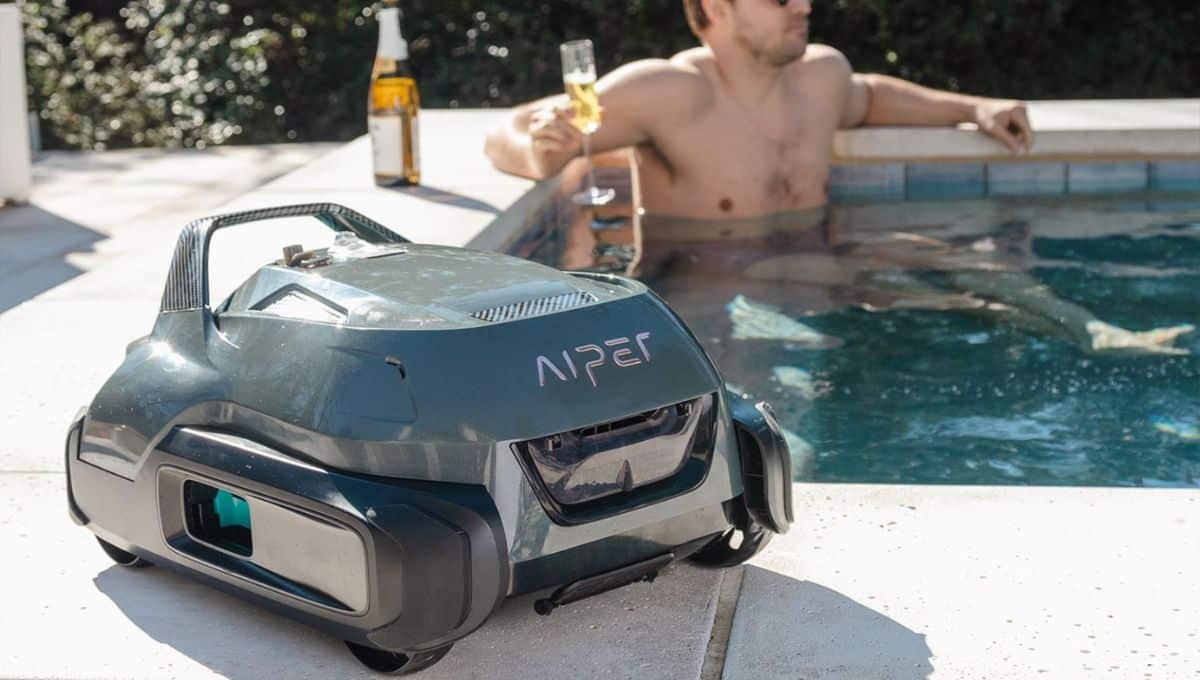 Man relaxing in a pool with a robotic pool cleaner at the edge of the pool