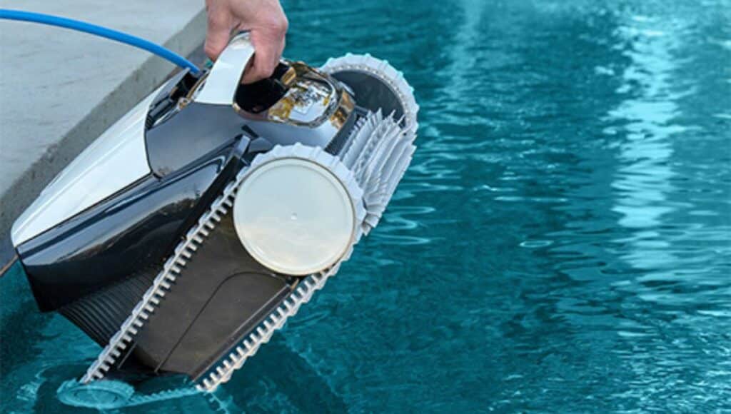A hand lifting up a robotic pool cleaner from a pool